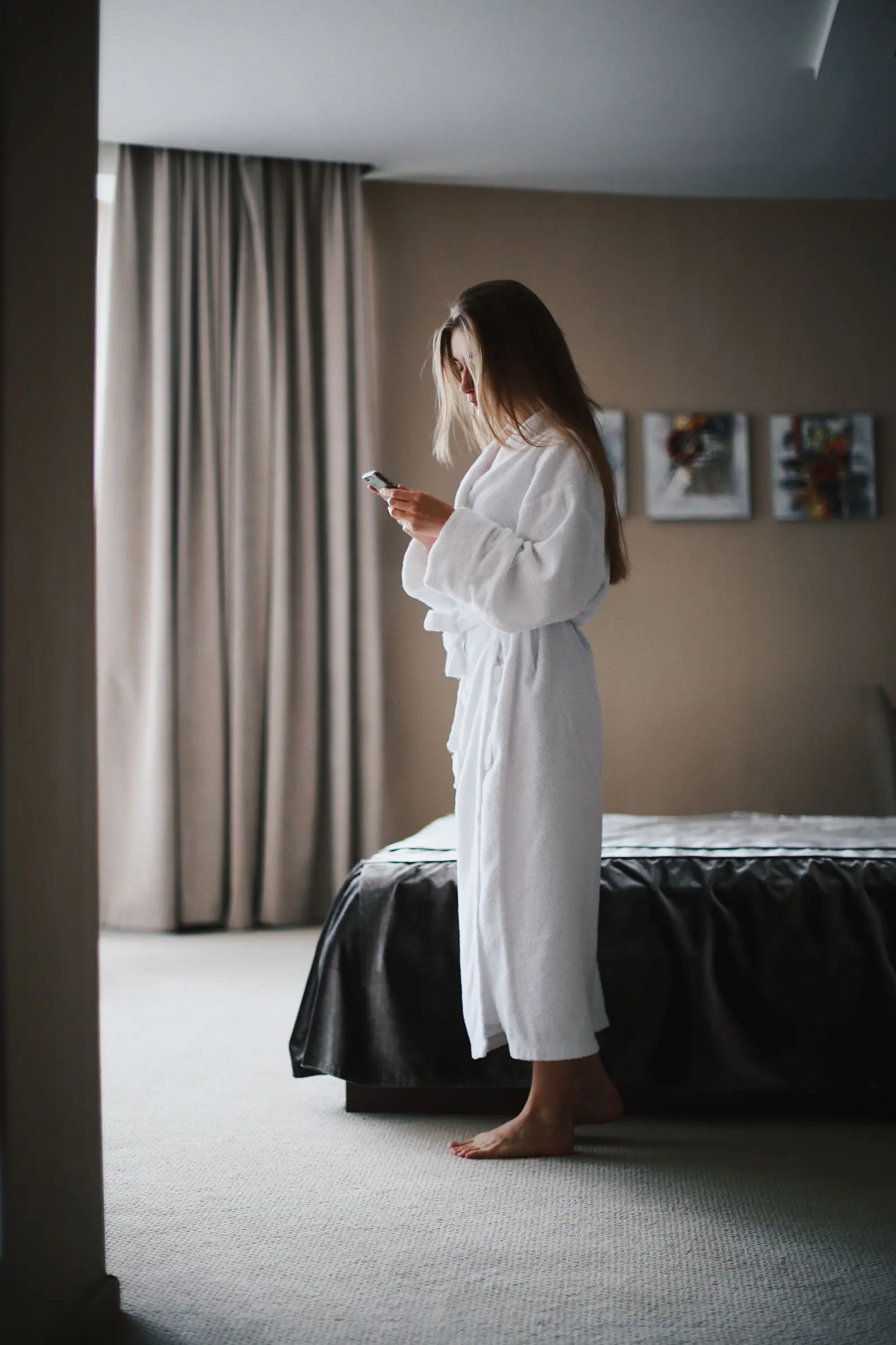 Woman in a white hotel robe looking at her phone in a hotel room