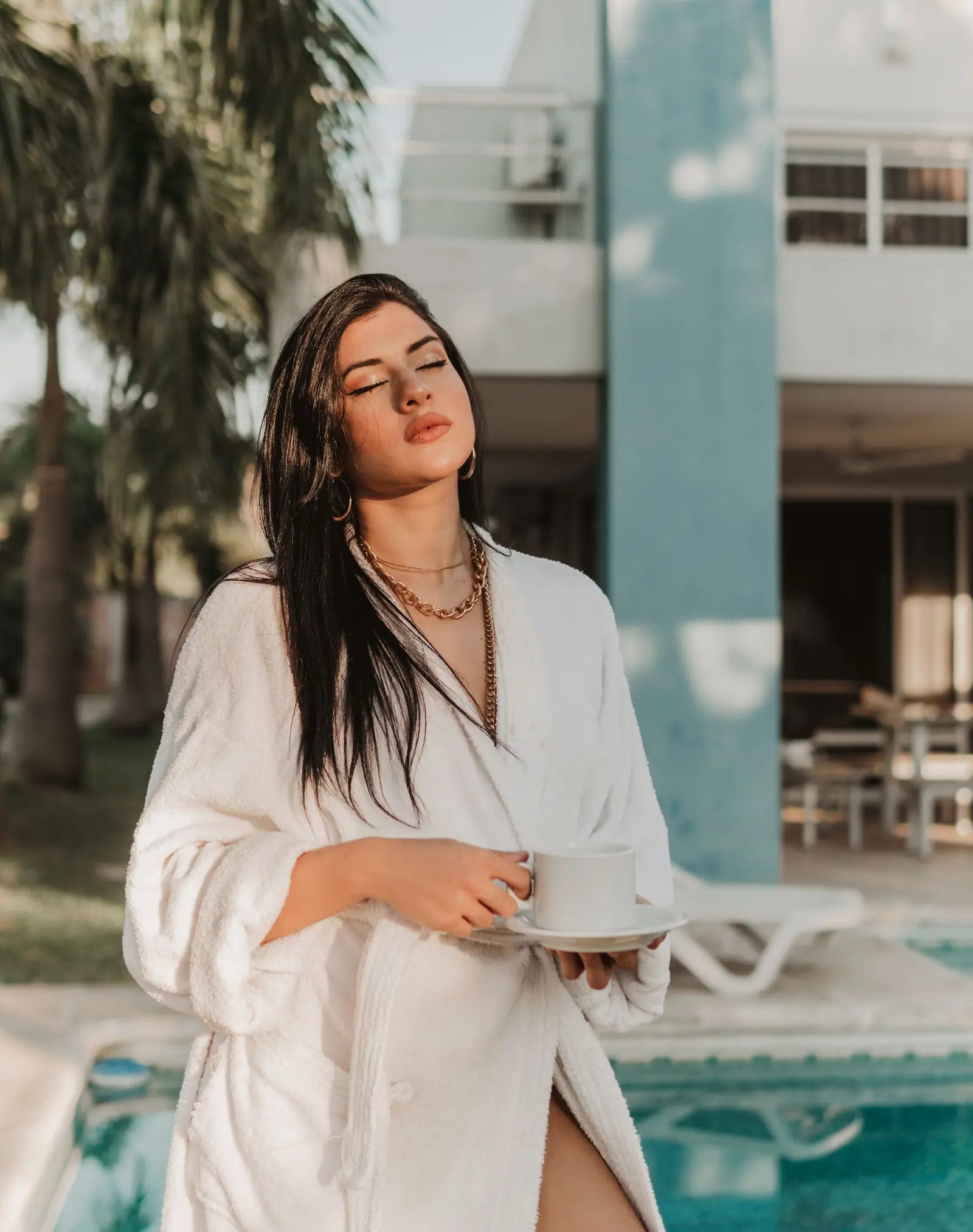 Woman in a white robe holding a cup of coffee by a pool