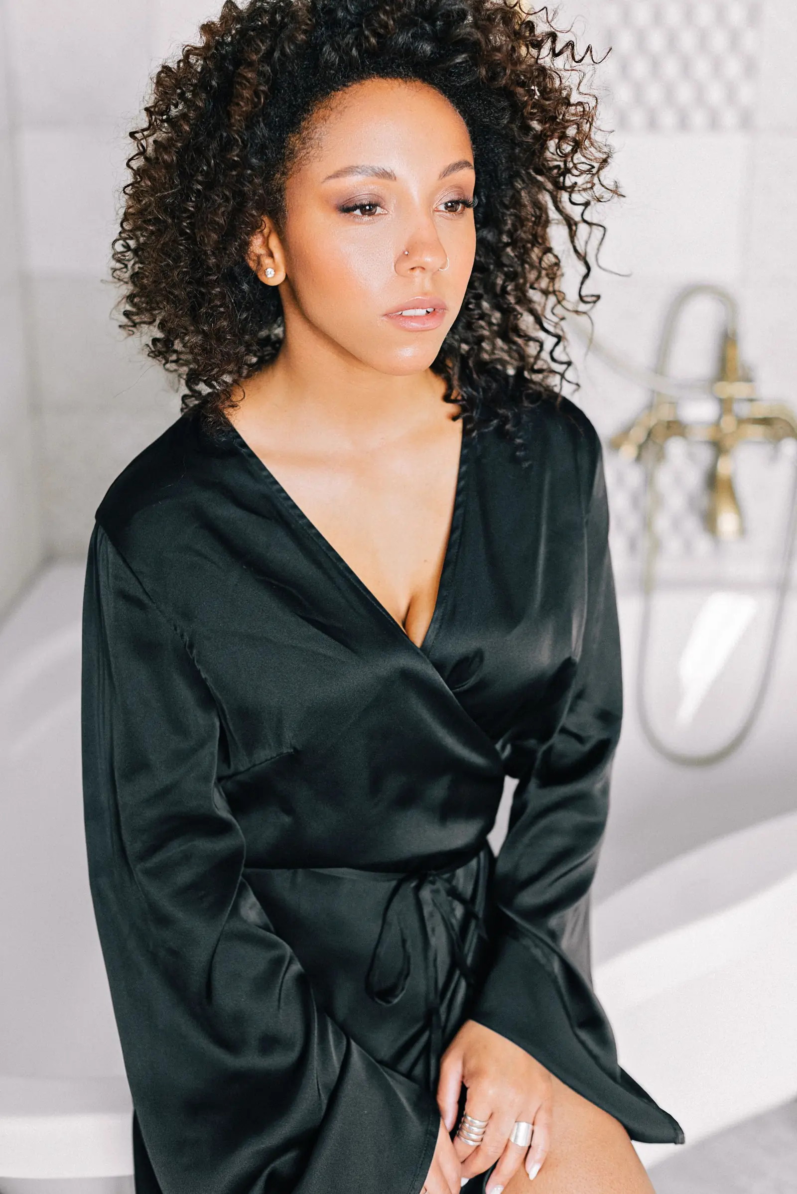 Woman with curly hair in a black satin robe in a bright bathroom