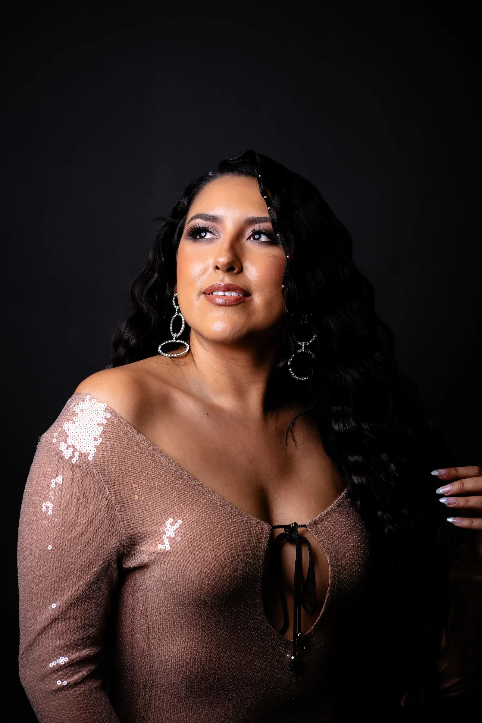 Woman with long dark wavy hair in an elegant sequined evening dress against a dark background
