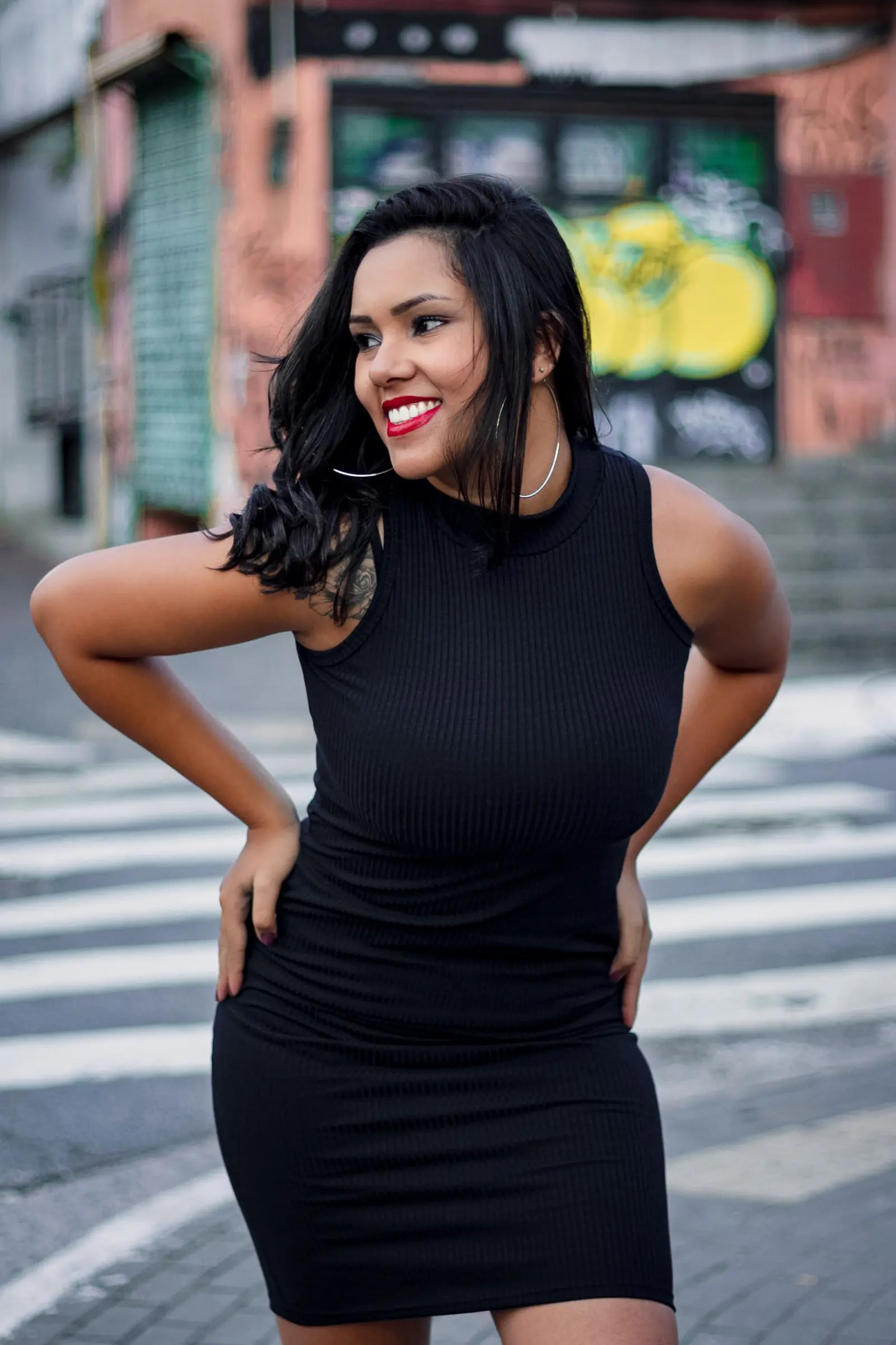Smiling woman with curly hair in a black dress on a city street